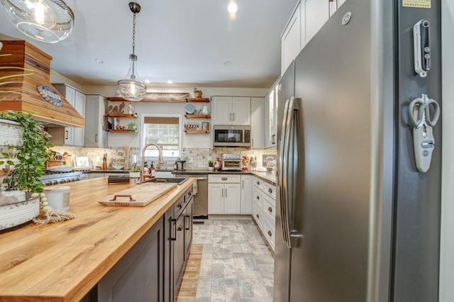 kitchen featuring pendant lighting, butcher block counters, stainless steel appliances, white cabinets, and decorative backsplash