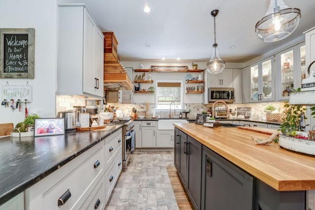 kitchen featuring butcher block countertops, sink, appliances with stainless steel finishes, hanging light fixtures, and white cabinets