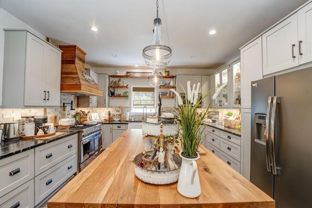 kitchen featuring pendant lighting, premium range hood, stainless steel appliances, white cabinets, and wood counters