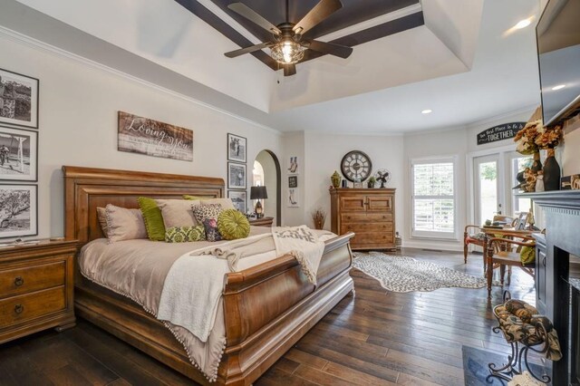 bedroom with a tray ceiling, a fireplace, ornamental molding, and dark wood-type flooring