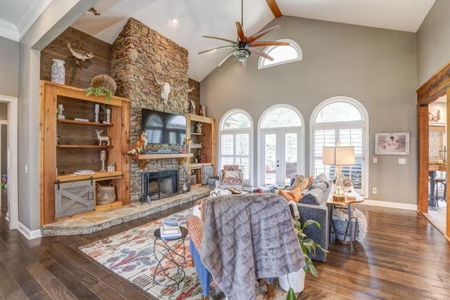 living room featuring dark wood-type flooring, ceiling fan, high vaulted ceiling, a stone fireplace, and french doors