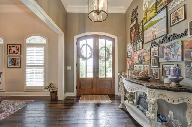 foyer entrance with an inviting chandelier, dark wood-type flooring, ornamental molding, and french doors