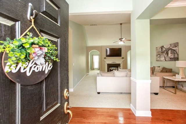 carpeted foyer entrance with ceiling fan, arched walkways, a fireplace, baseboards, and wood finished floors