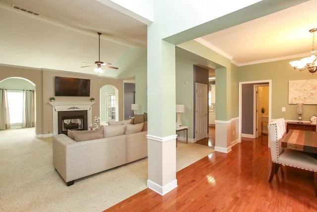 living room featuring arched walkways, ceiling fan, a chandelier, a multi sided fireplace, and crown molding