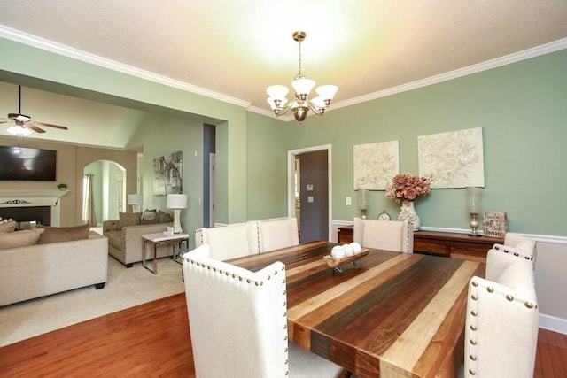 dining space with a chandelier, wood finished floors, crown molding, arched walkways, and ceiling fan