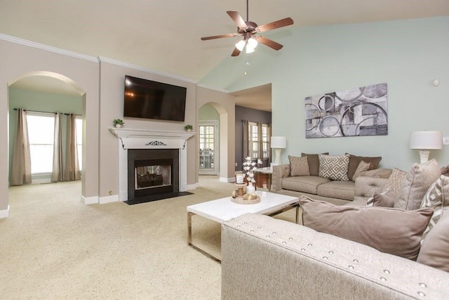 carpeted living room featuring arched walkways, a ceiling fan, a fireplace with flush hearth, baseboards, and high vaulted ceiling