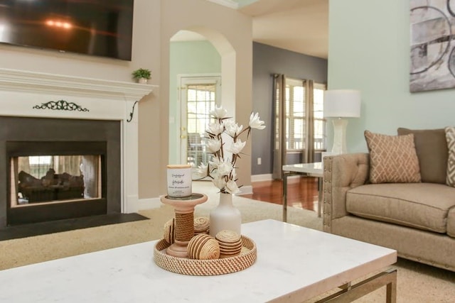 living area featuring a multi sided fireplace, arched walkways, baseboards, and carpet flooring