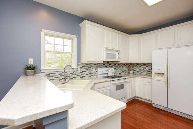 kitchen featuring white appliances, a sink, a peninsula, tasteful backsplash, and dark wood-style flooring