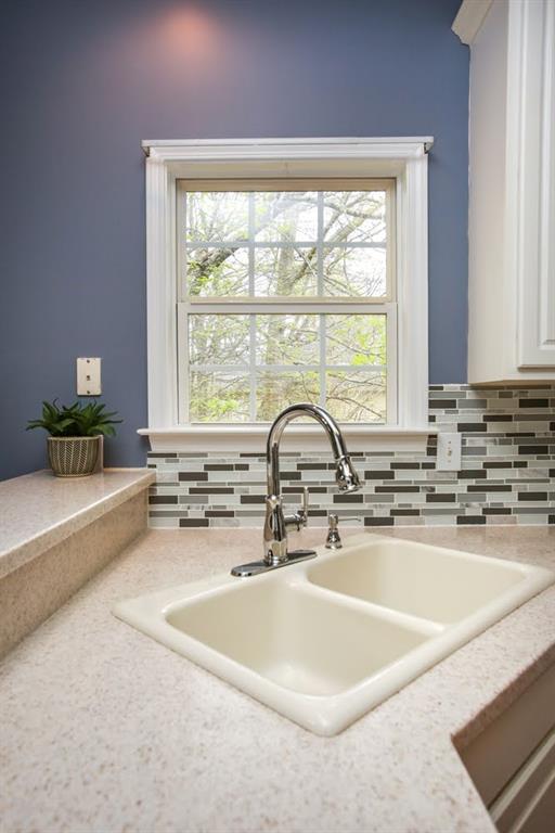kitchen view of a sink, light countertops, decorative backsplash, and white cabinets