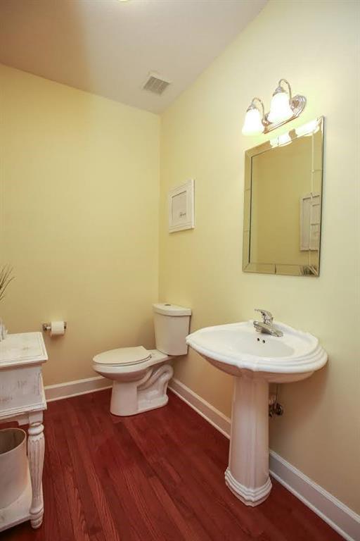 half bath featuring wood finished floors, baseboards, and toilet