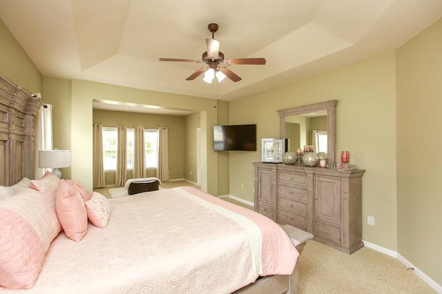 bedroom with a raised ceiling, light carpet, baseboards, and ceiling fan