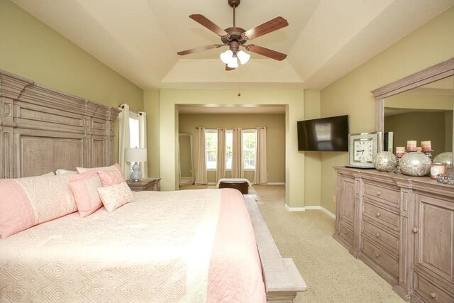 bedroom featuring light carpet, a tray ceiling, baseboards, and ceiling fan