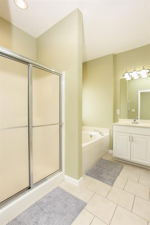 full bath featuring tile patterned flooring, a bath, vanity, and a stall shower