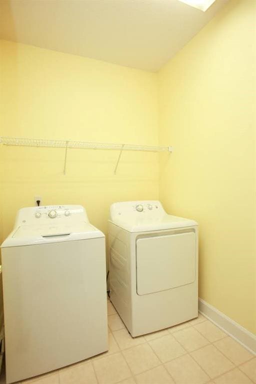 washroom with washer and dryer, light tile patterned flooring, and baseboards