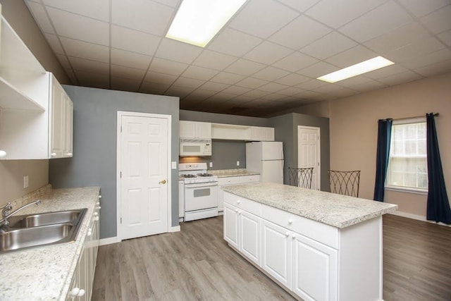 kitchen featuring white appliances, a sink, light wood-style floors, a center island, and a paneled ceiling