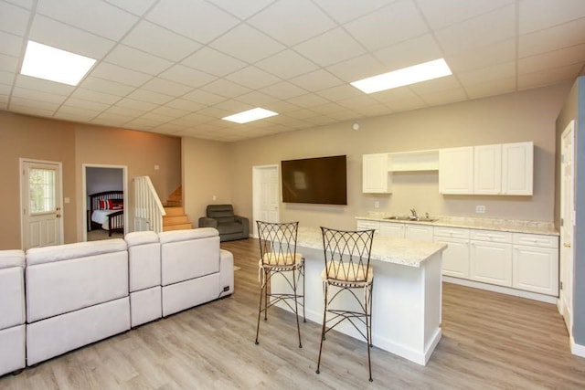 living area featuring light wood-style flooring, a drop ceiling, and baseboards
