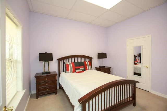 bedroom featuring light colored carpet, a paneled ceiling, and baseboards