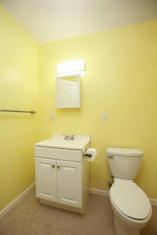 half bath featuring tile patterned floors, toilet, baseboards, and vanity