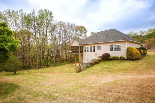 back of house featuring a sunroom, a lawn, and a shingled roof