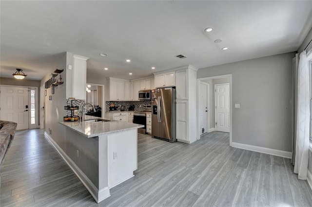 kitchen with kitchen peninsula, appliances with stainless steel finishes, tasteful backsplash, sink, and white cabinetry