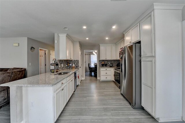 kitchen with kitchen peninsula, appliances with stainless steel finishes, light stone counters, sink, and white cabinetry