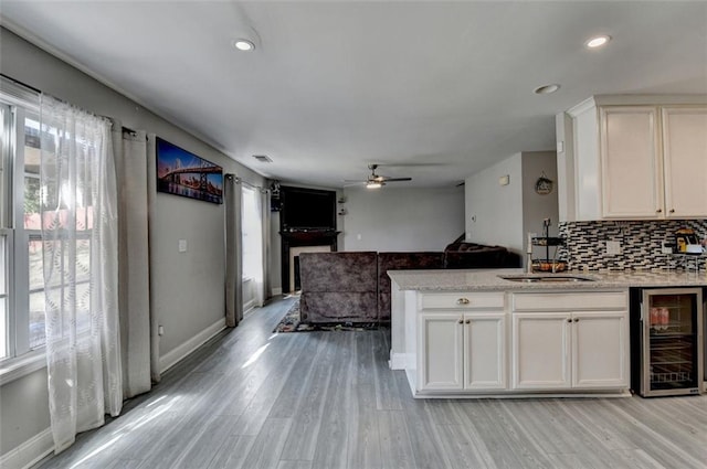 kitchen with wine cooler, white cabinetry, sink, and light hardwood / wood-style flooring