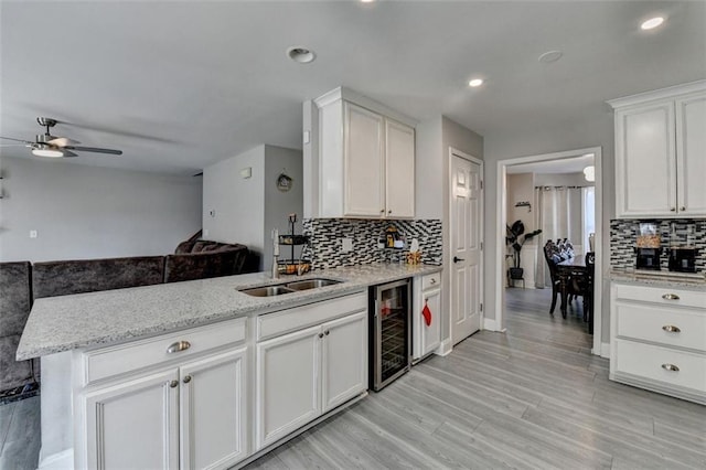 kitchen with kitchen peninsula, sink, wine cooler, light stone counters, and white cabinetry