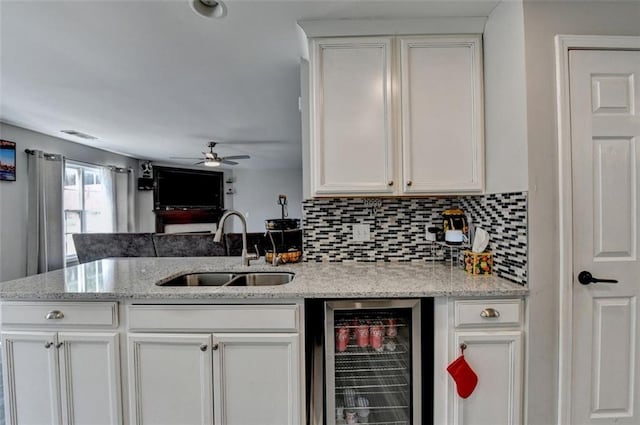 kitchen with light stone countertops, white cabinetry, sink, ceiling fan, and beverage cooler