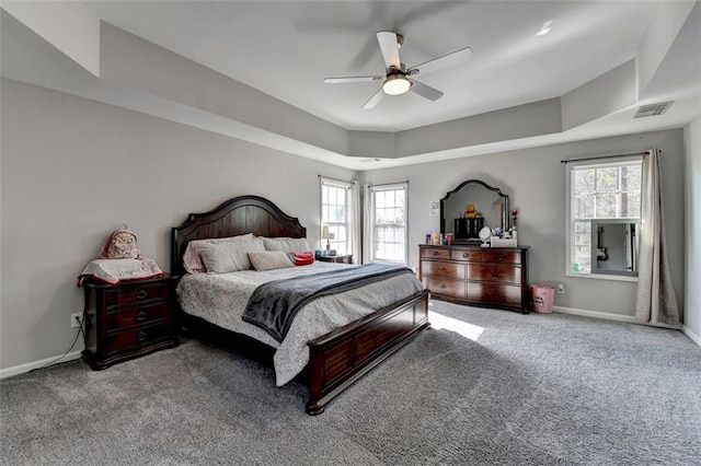 carpeted bedroom with multiple windows, a raised ceiling, and ceiling fan