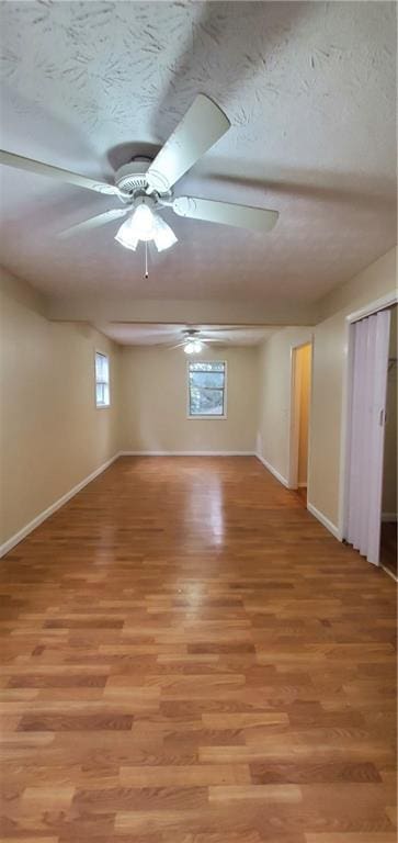 spare room featuring light wood-type flooring, baseboards, a textured ceiling, and ceiling fan