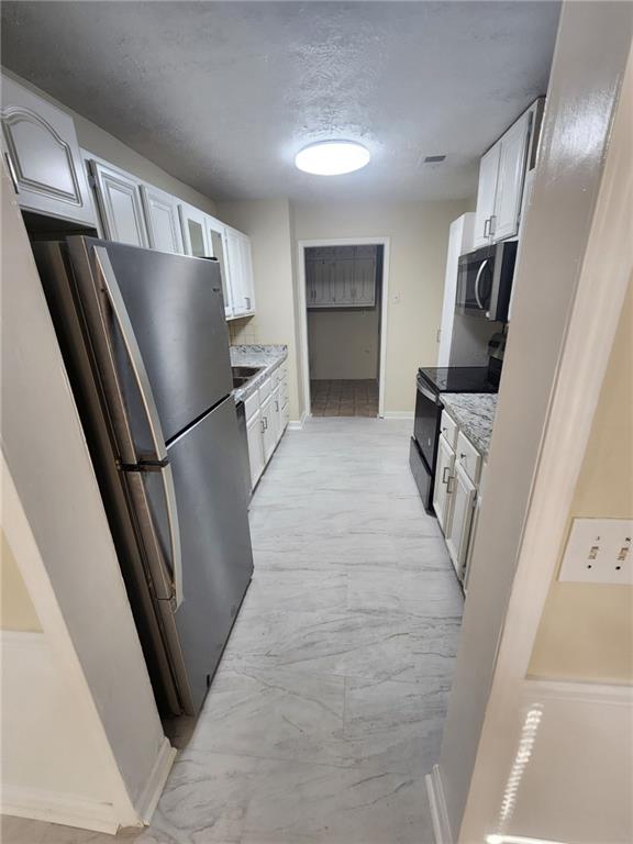 kitchen featuring baseboards, stainless steel appliances, a textured ceiling, white cabinetry, and marble finish floor