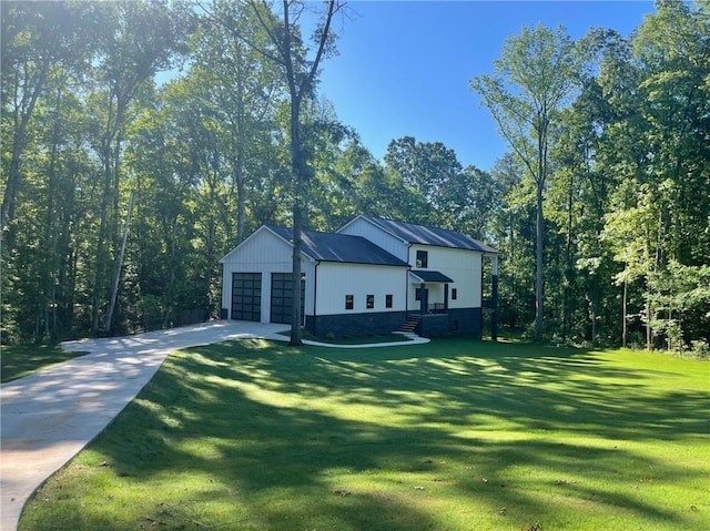 view of side of property with a garage, stone siding, a lawn, and driveway