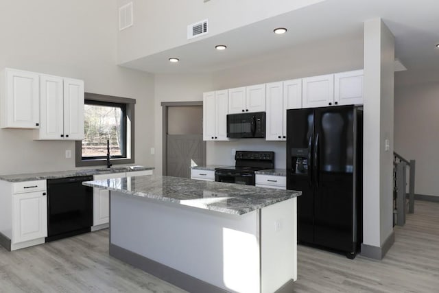 kitchen featuring stone counters, black appliances, white cabinets, light hardwood / wood-style floors, and a kitchen island