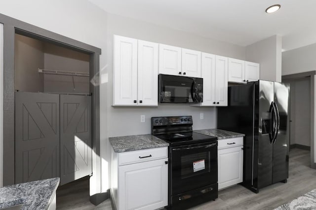 kitchen with black appliances, wood-type flooring, white cabinetry, and dark stone counters