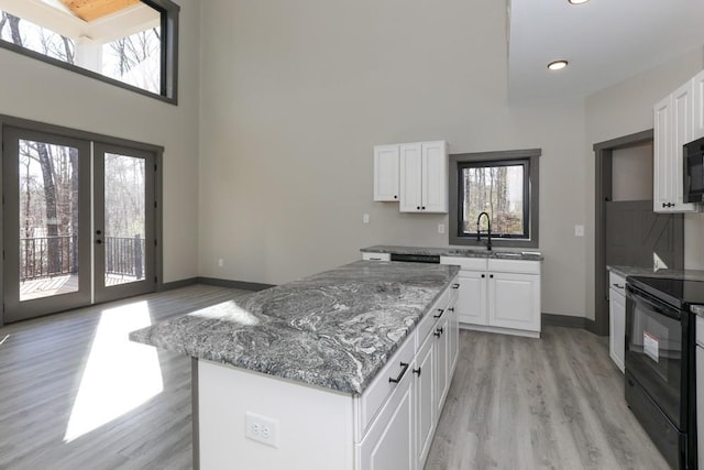 kitchen featuring light stone countertops, a center island, sink, white cabinets, and black appliances