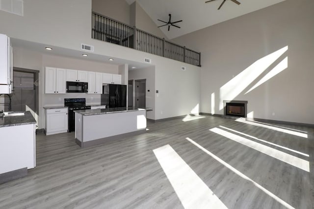 kitchen with a center island, sink, a towering ceiling, white cabinets, and black appliances