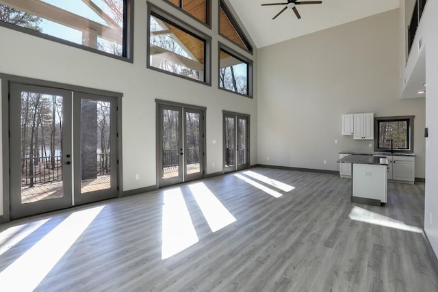 unfurnished living room featuring ceiling fan, wood-type flooring, high vaulted ceiling, and french doors