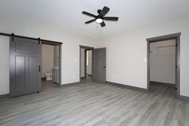 unfurnished bedroom featuring ensuite bath, a spacious closet, ceiling fan, a barn door, and a closet