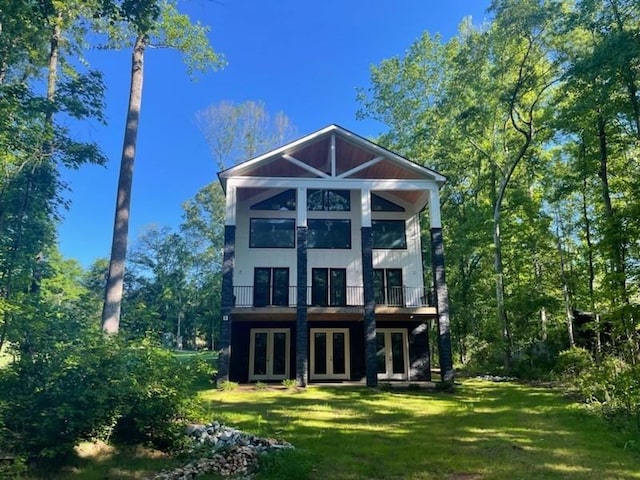 rear view of property featuring a yard, french doors, and a balcony