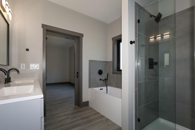 full bathroom featuring double vanity, wood finished floors, a garden tub, a shower stall, and a sink