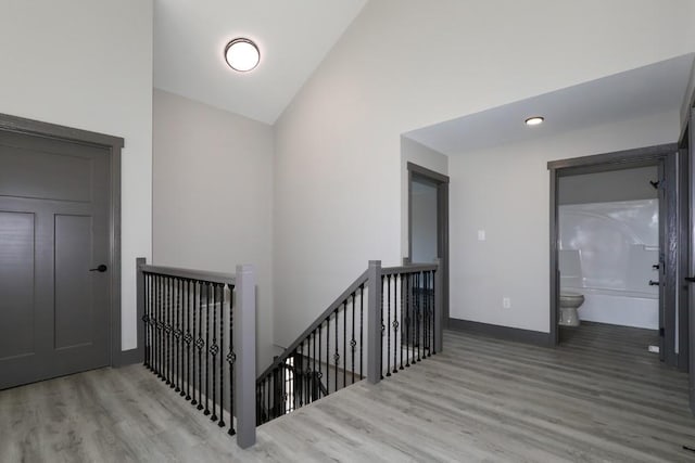 hall featuring high vaulted ceiling, baseboards, wood finished floors, and an upstairs landing