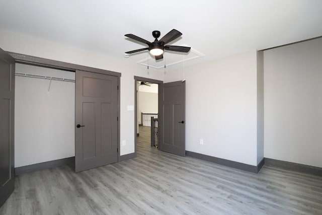 unfurnished bedroom with light wood-type flooring, attic access, baseboards, and ceiling fan