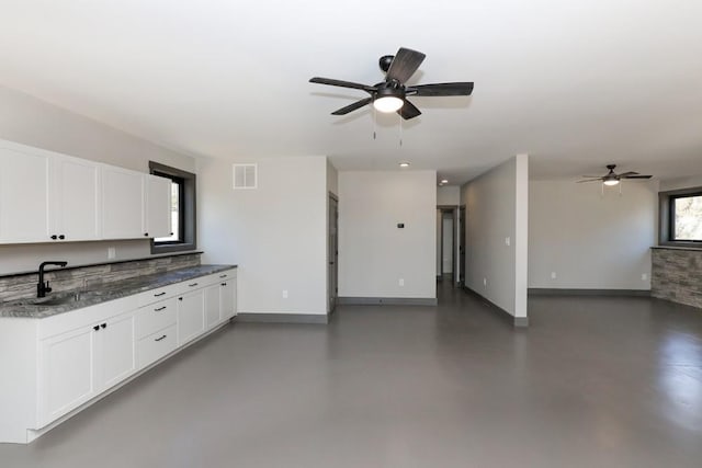 kitchen with white cabinets, a healthy amount of sunlight, dark stone counters, and sink