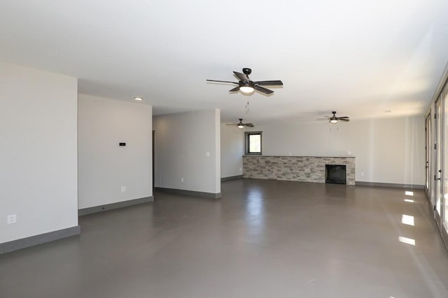 unfurnished living room with concrete flooring, ceiling fan, a fireplace, and baseboards