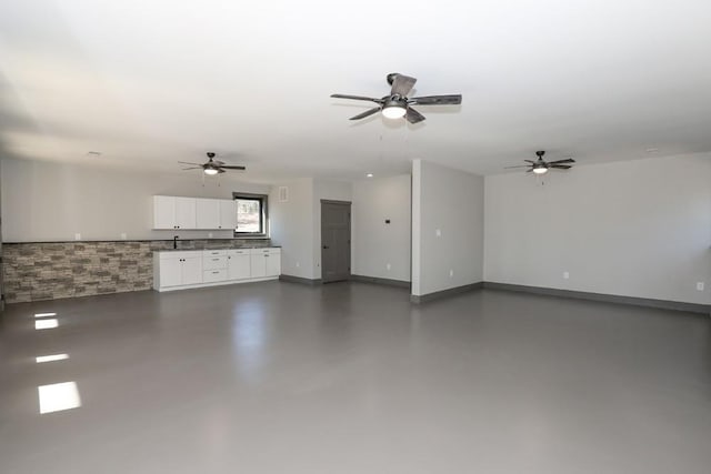 unfurnished living room with finished concrete floors, a sink, baseboards, and ceiling fan