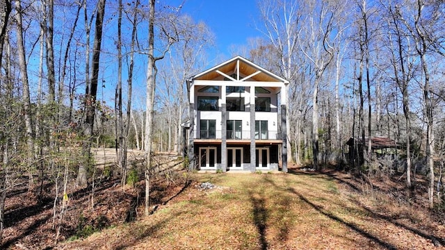 rear view of house with a balcony, stucco siding, a view of trees, and a yard