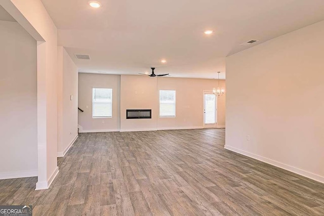 unfurnished living room featuring ceiling fan with notable chandelier, wood-type flooring, and a healthy amount of sunlight