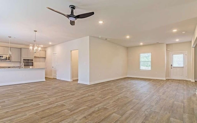 unfurnished living room featuring ceiling fan with notable chandelier, sink, and light hardwood / wood-style floors