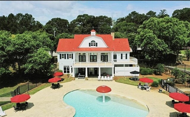 rear view of house with a fenced in pool, a balcony, and a patio area
