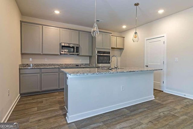 kitchen with light stone counters, decorative light fixtures, a kitchen island with sink, and stainless steel appliances